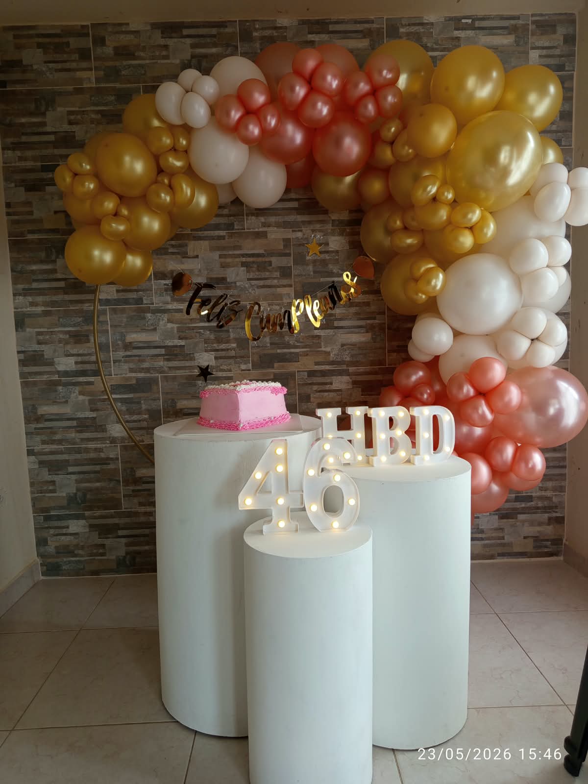 Arco de globos dorado, blanco y coral con letras HBD iluminadas